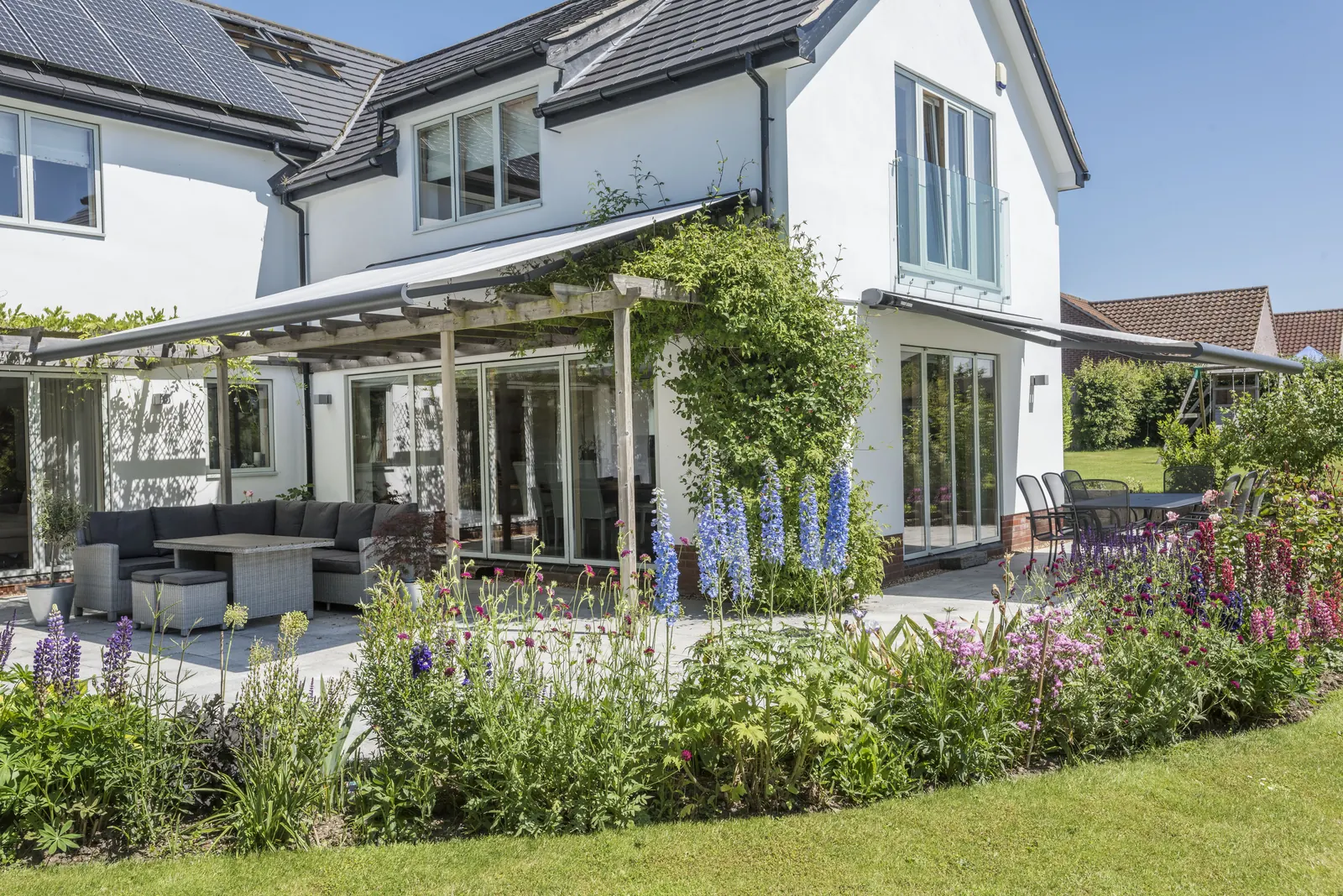 Garden with deep flowering borders, lawn and a covered patio